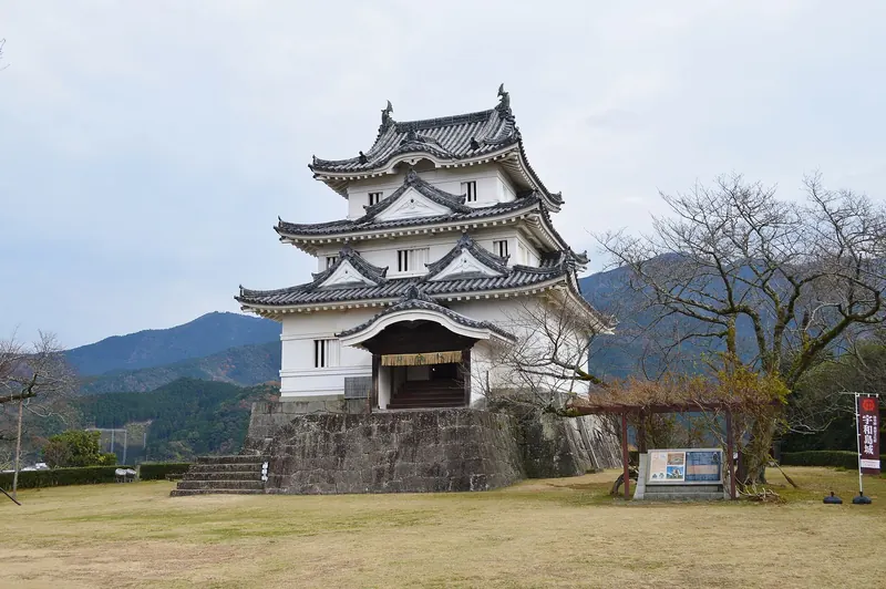 The small white keep of Uwajima Castle on a lawn with hills behind
