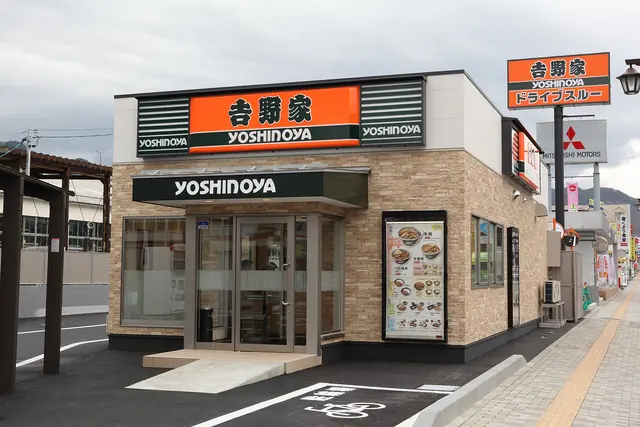 A small Yoshinoya restaurant with an orange sign above glass doors and a menu board beside the entrance