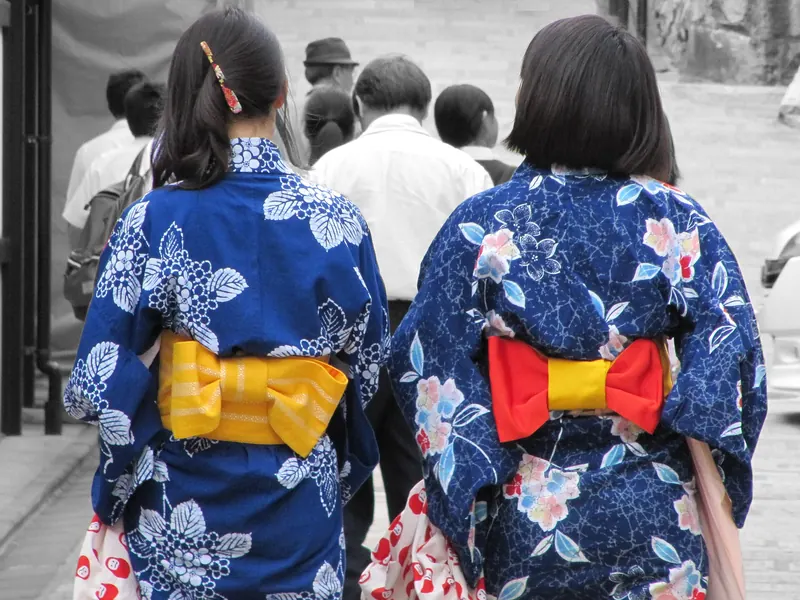 Two people in dark-blue flowered yukata with yellow and red obi bows, seen from behind